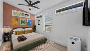 Un dormitorio moderno con cama, ventilador de techo, obras de arte, ventanas y un equipo de aire acondicionado integrado.