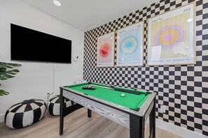 A pool table with a checkered wall and framed artwork.