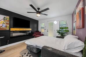 Ein modernes Schlafzimmer mit Bett, Wand-Fernseher, Deckenventilator und einer Tür mit Frostglas.
