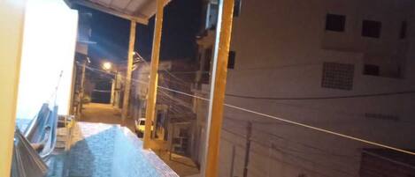 Un espacio al aire libre techado con piso de baldosas, pilares de madera y vistas a edificios cercanos.