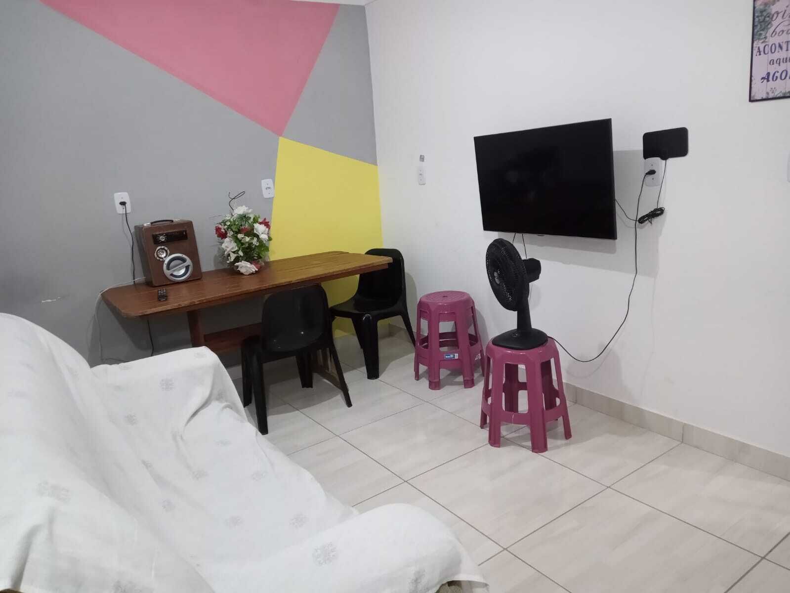 A room with a bed, a desk with a radio, a TV, and two pink stools.