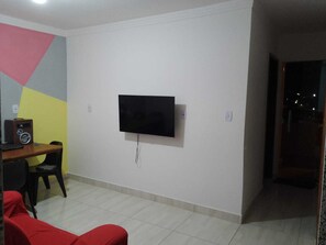 Sala de estar com TV de tela plana na parede, escrivaninha de madeira com rádio e sofá vermelho.