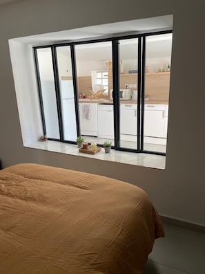 A bedroom with a large window overlooking a kitchen.