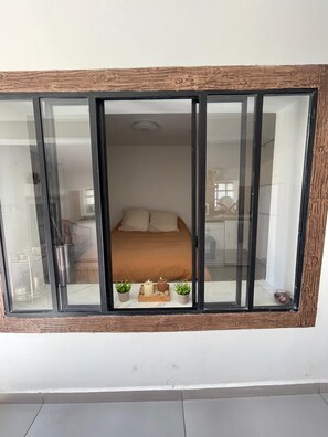 A room with a bed, a window with a wooden frame, and a small table with candles and plants. - Vrbo Property (Berre-l'Étang)