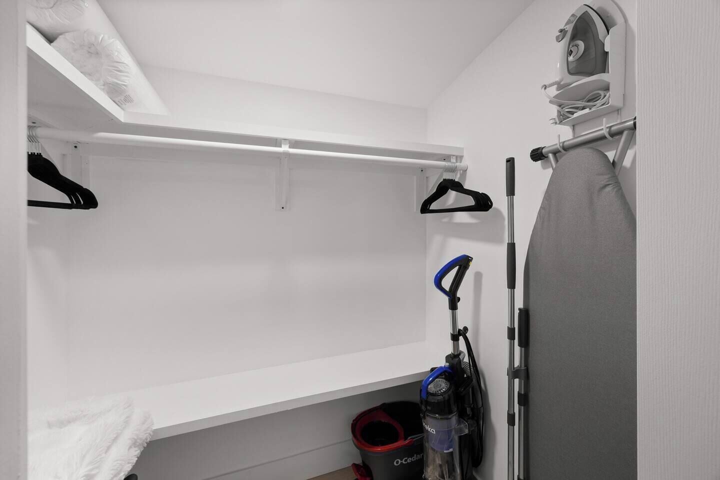 Un placard avec une tringle pour suspendre les vêtements, un aspirateur et un panier à linge.