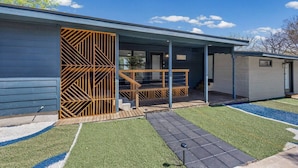 A modern building with a covered porch, a wooden fence, and a well-maintained lawn. - Music Themed BNB | Disco Lights | Fire Pit Lounge (Austin)