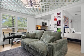 Una sala moderna con un sofá gris, un comedor con mesa y sillas, una cocina con microondas y un dormitorio con cama.