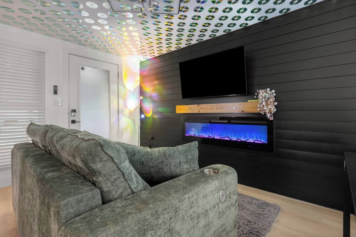 A modern living room with a grey sofa, a flat-screen TV mounted on a black wall, and a decorative fish tank.