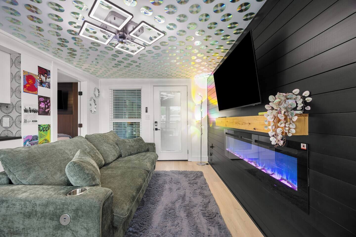 Un salon moderne avec un canapé vert, un téléviseur à écran plat fixé sur un mur noir et un aquarium décoratif.