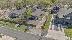 A residential area with houses, a road, and a fenced yard with a playground. - Music Themed BNB | Disco Lights | Fire Pit Lounge (Austin)