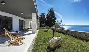 A modern outdoor seating area with lounge chairs and a stone wall overlooking a body of water. - Villa Jadranka - Private villa with pool (Borak)