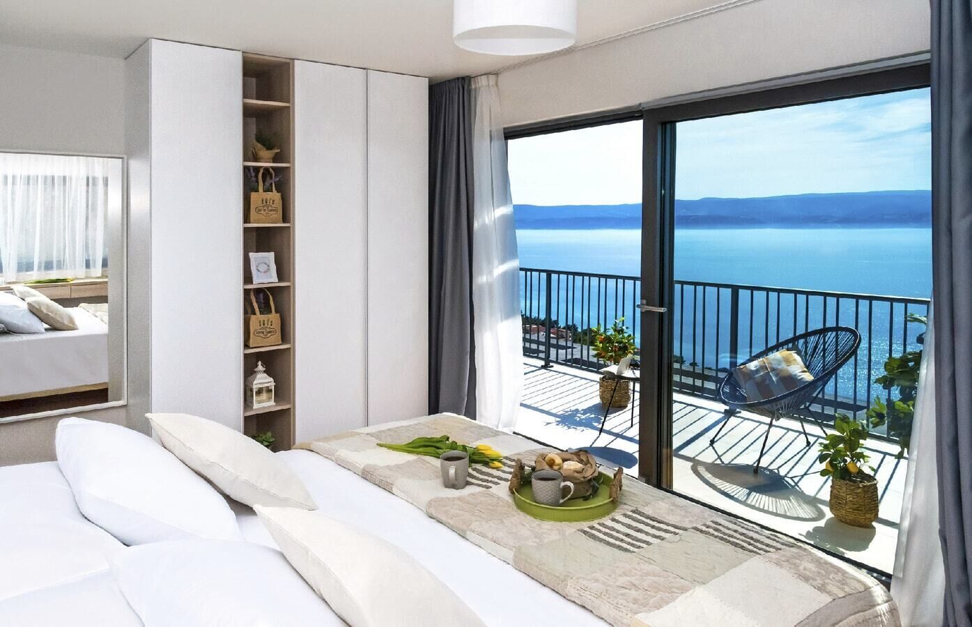 A modern bedroom with a balcony, a bed, a bedside table with breakfast items, and a view of the sea.