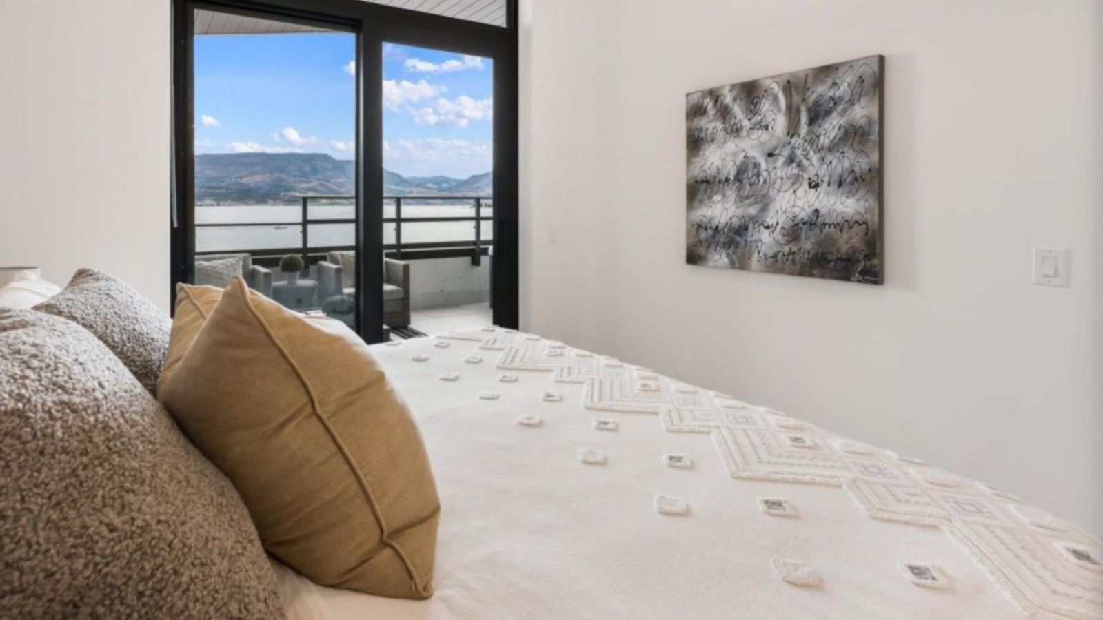Ein Schlafzimmer mit einem Bett, Kissen, Seeblick und einem Gemälde an der Wand.