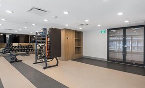 Ein Fitnessraum mit Trainingsgeräten, einem an der Wand befestigten Hantelständer und einer Tür zu einem weiteren Raum.