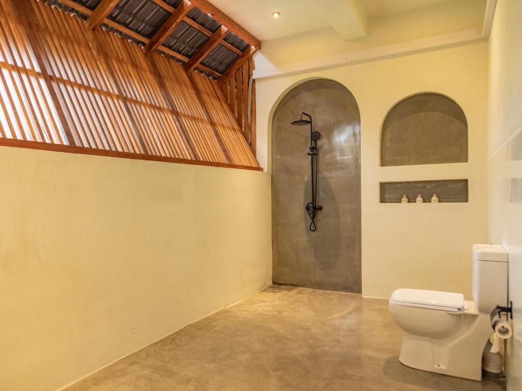 A bathroom with a shower, a toilet, and a wooden ceiling.
