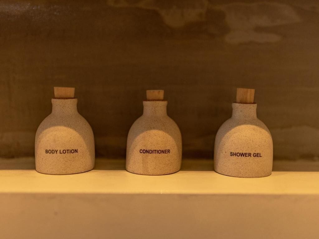 Tres botellas etiquetadas como loción corporal, acondicionador y gel de ducha sobre una repisa.