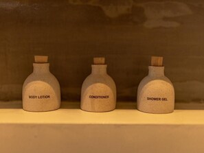 Three bottles labeled body lotion, conditioner, and shower gel on a shelf.