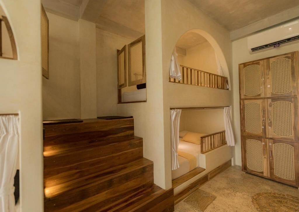 Una escalera conduce a una zona con literas, un armario de madera y un ventanal.
