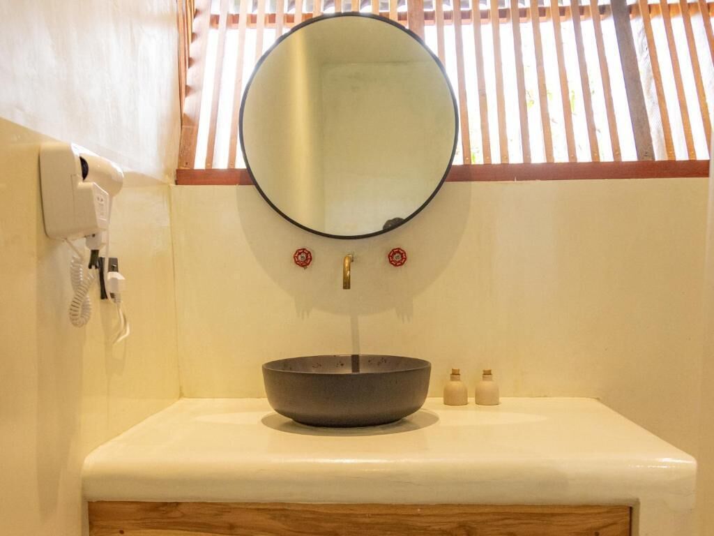Un baño con un espejo redondo, un lavabo y un teléfono en la pared.