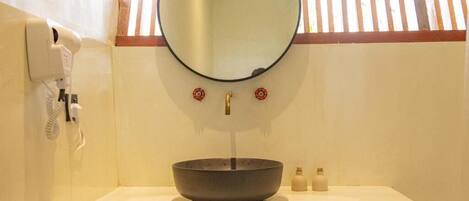 Un baño con un espejo redondo, un lavabo y un teléfono en la pared.