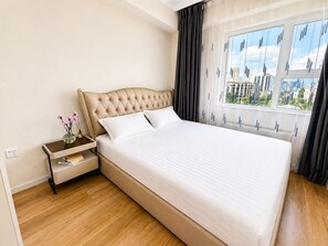 Een hotelkamer met een groot bed, een nachtkastje met een bloevas en een raam met uitzicht op de stad.