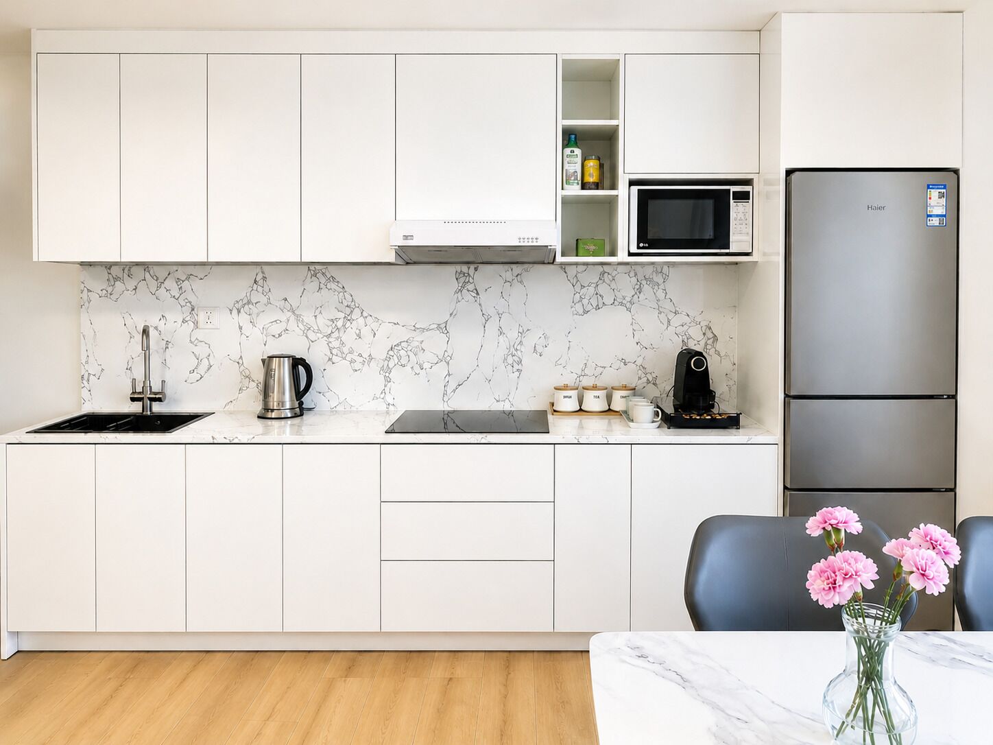 A modern kitchen with white cabinets, a stainless steel refrigerator, a microwave, and a coffee maker.