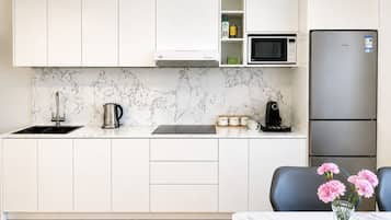 A modern kitchen with white cabinets, a stainless steel refrigerator, a microwave, and a coffee maker.