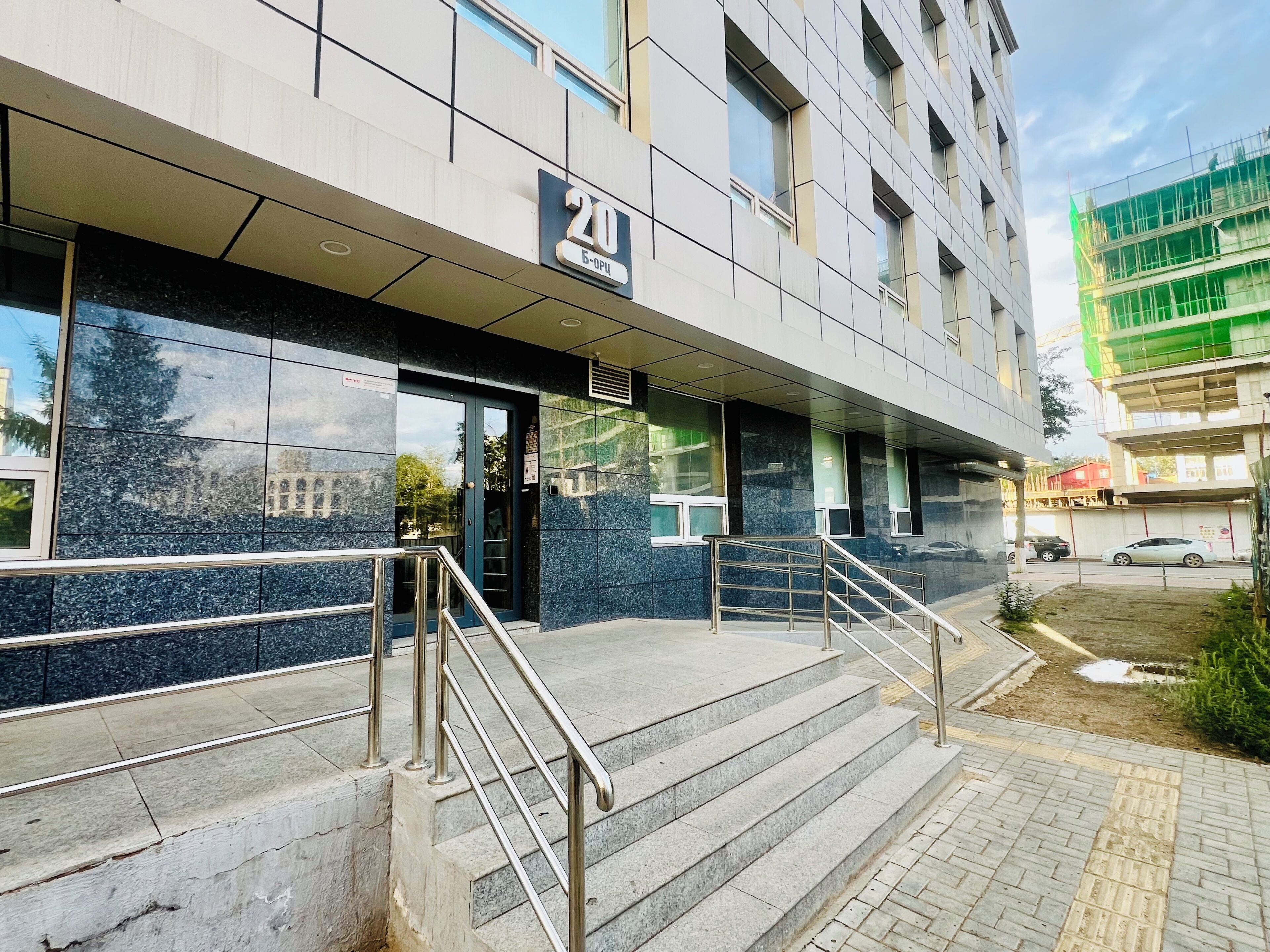 A building with a sign indicating the number 20, a set of stairs with metal railings, and a paved entrance area.
