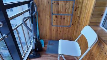 Een kleine kamer met een houten wand, een raam, een witte stoel en een stofzuiger.