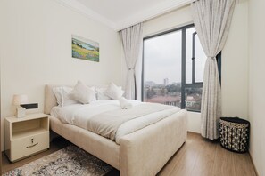 Ein Schlafzimmer mit Bett, Nachttisch, Lampe und Blick auf die Stadt durch ein Fenster.
