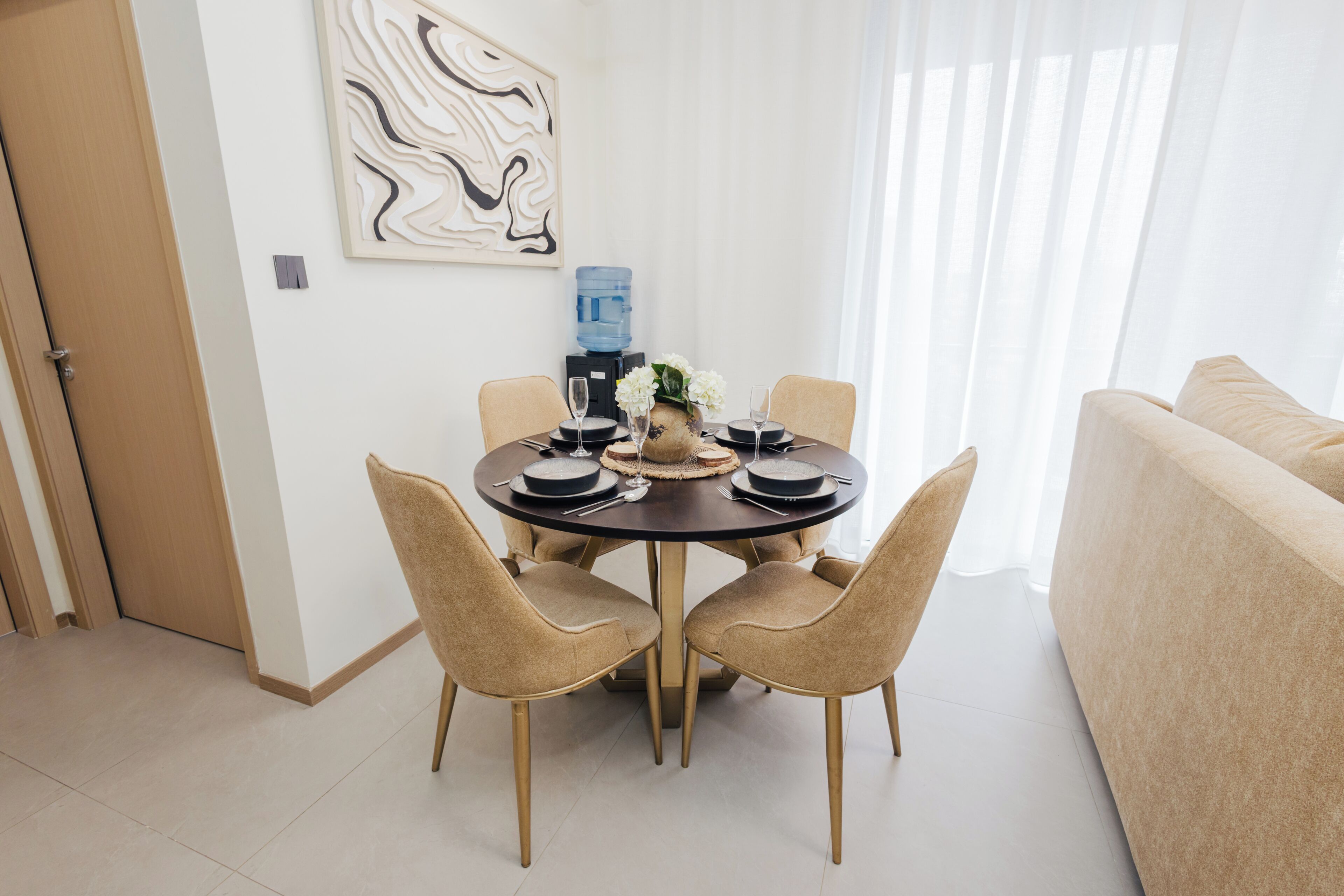 Un coin repas comprenant une table ronde, quatre chaises, un distributeur d’eau et un élément décoratif mural.