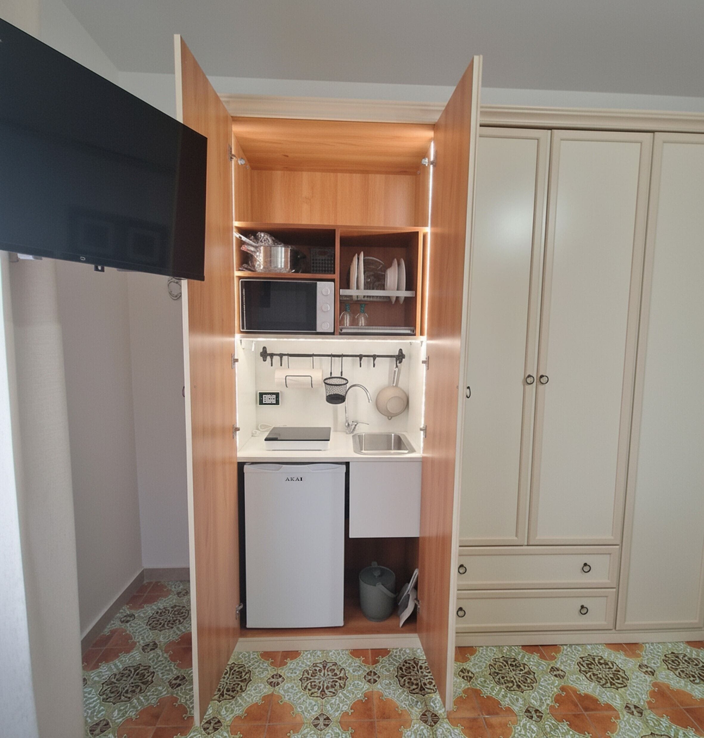 Una kitchenette compacta con microondas, lavamanos y armarios de almacenamiento.