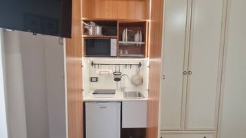 Una kitchenette compacta con microondas, lavamanos y armarios de almacenamiento.