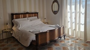 Et hotelværelse med en stor seng, et rundt spejl og udsigt gennem lette gardiner.