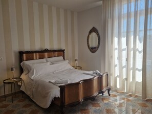 A hotel room with a large bed, a round mirror, and a view through sheer curtains. - B&B il 900 (Avezzano)