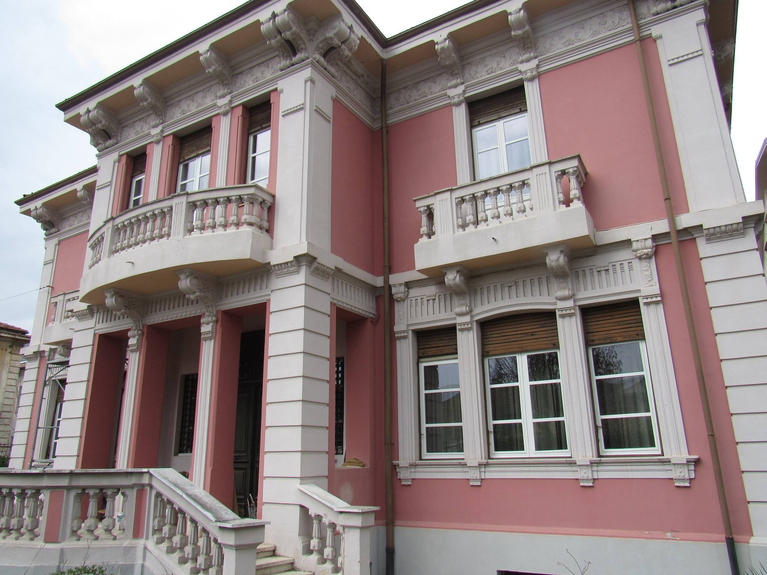 Un edificio con fachada rosa, detalles blancos y balcones ornamentados.
