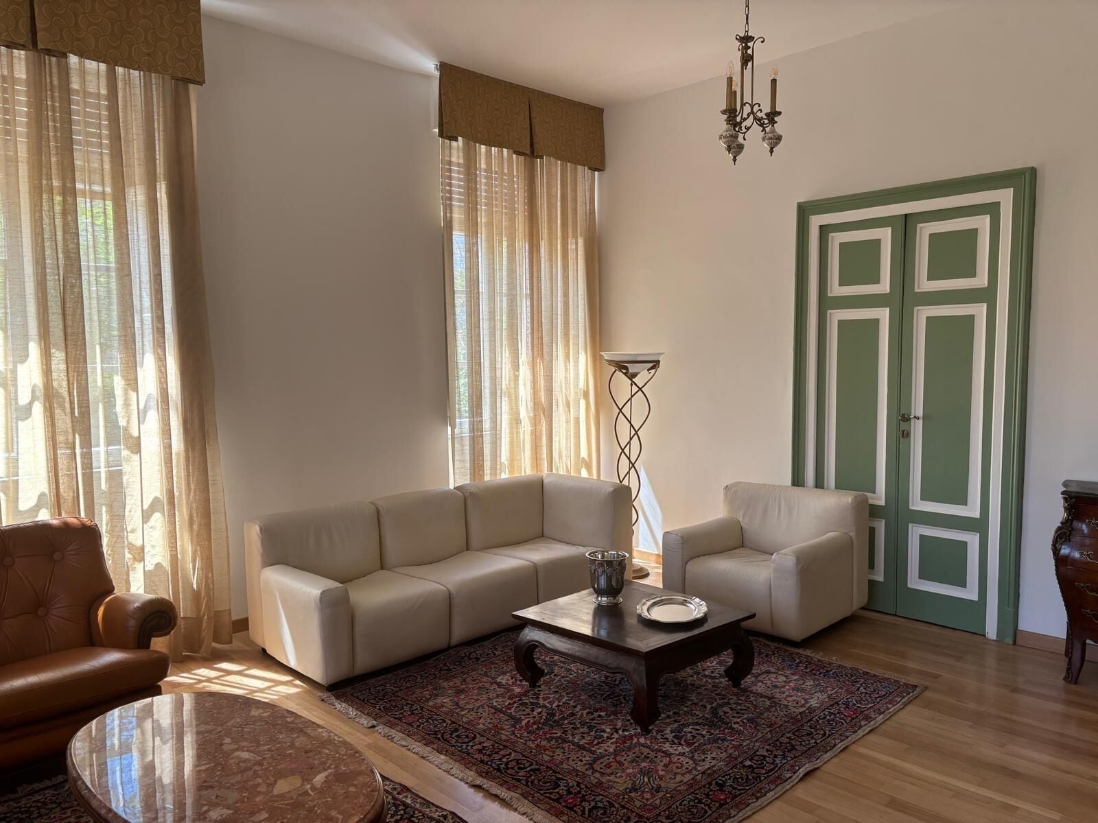 A living room with a beige sofa, a coffee table, a floor lamp, a patterned rug, and a green door.