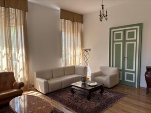 A living room with a beige sofa, a coffee table, a floor lamp, a patterned rug, and a green door. - B&B il 900 (Avezzano)