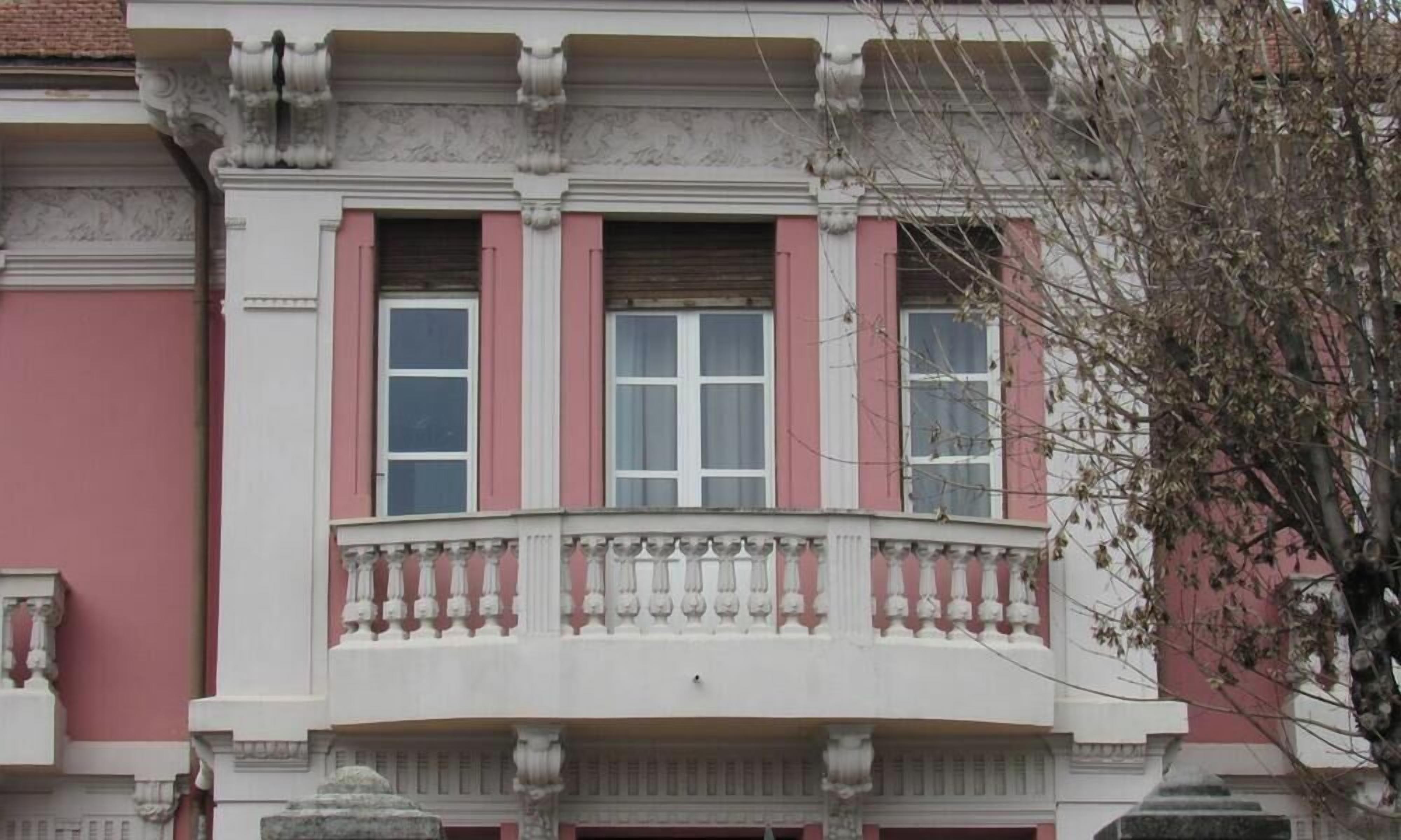 A building with a balcony, a window with shutters, and a decorative balustrade.