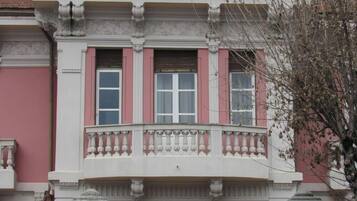 A building with a balcony, a window with shutters, and a decorative balustrade.