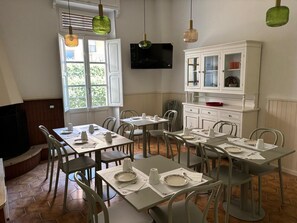 A dining area with multiple tables and chairs, a television mounted on the wall, and a cabinet with glass doors. - B&B il 900 (Avezzano)