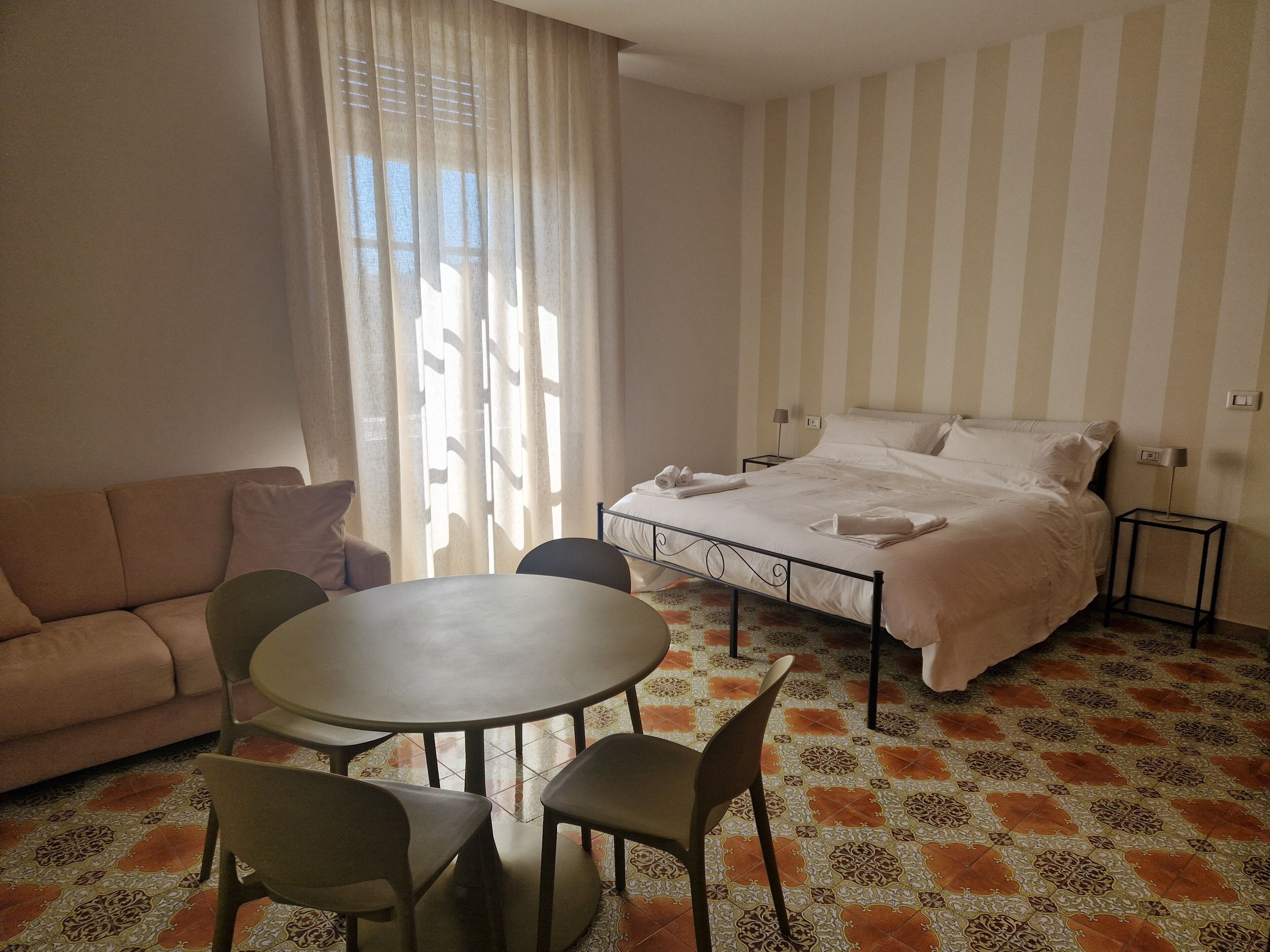 Une chambre d’hôtel avec un lit, un canapé, une table à manger avec des chaises et un sol à motifs.