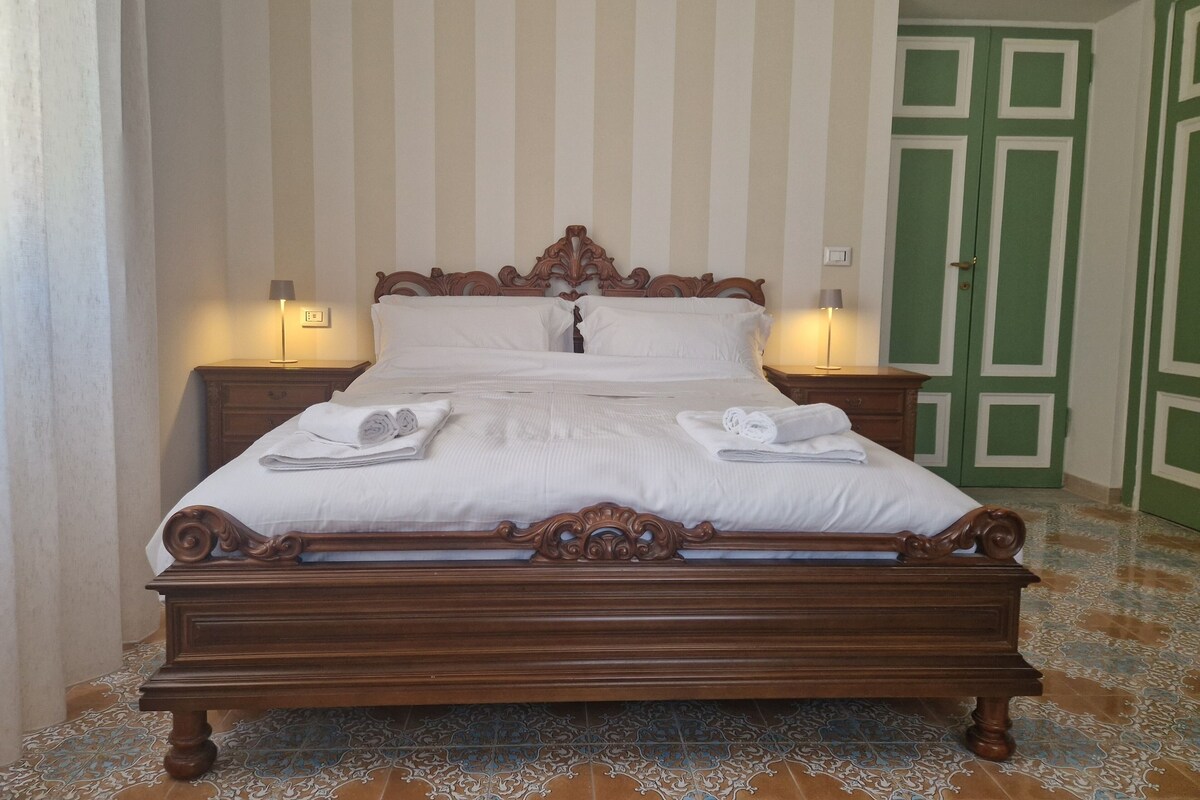 A neatly made bed with pillows and towels, two bedside lamps, and a green door in the background.