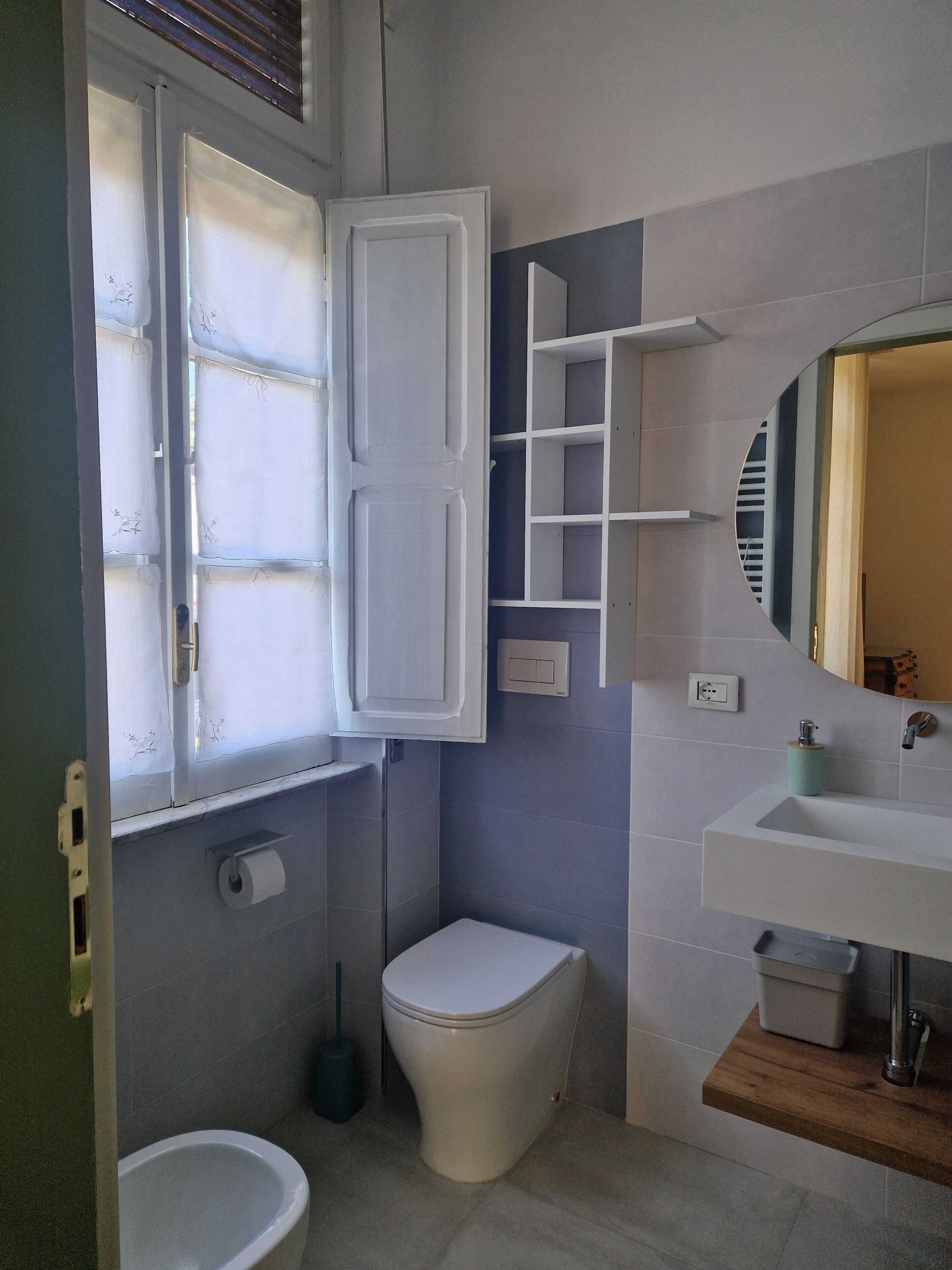 Une salle de bain avec des toilettes, un lavabo, un miroir et une fenêtre avec des rideaux.