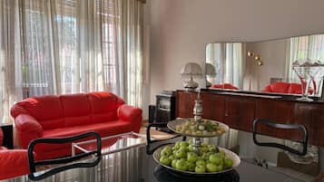 Un salon avec un canapé rouge, une table basse en verre sur laquelle sont posées des pommes, et un meuble en bois.