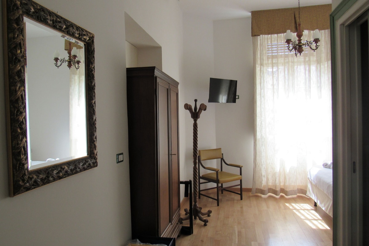 A room with a large mirror, a wardrobe, a television, a chair, and a bed.