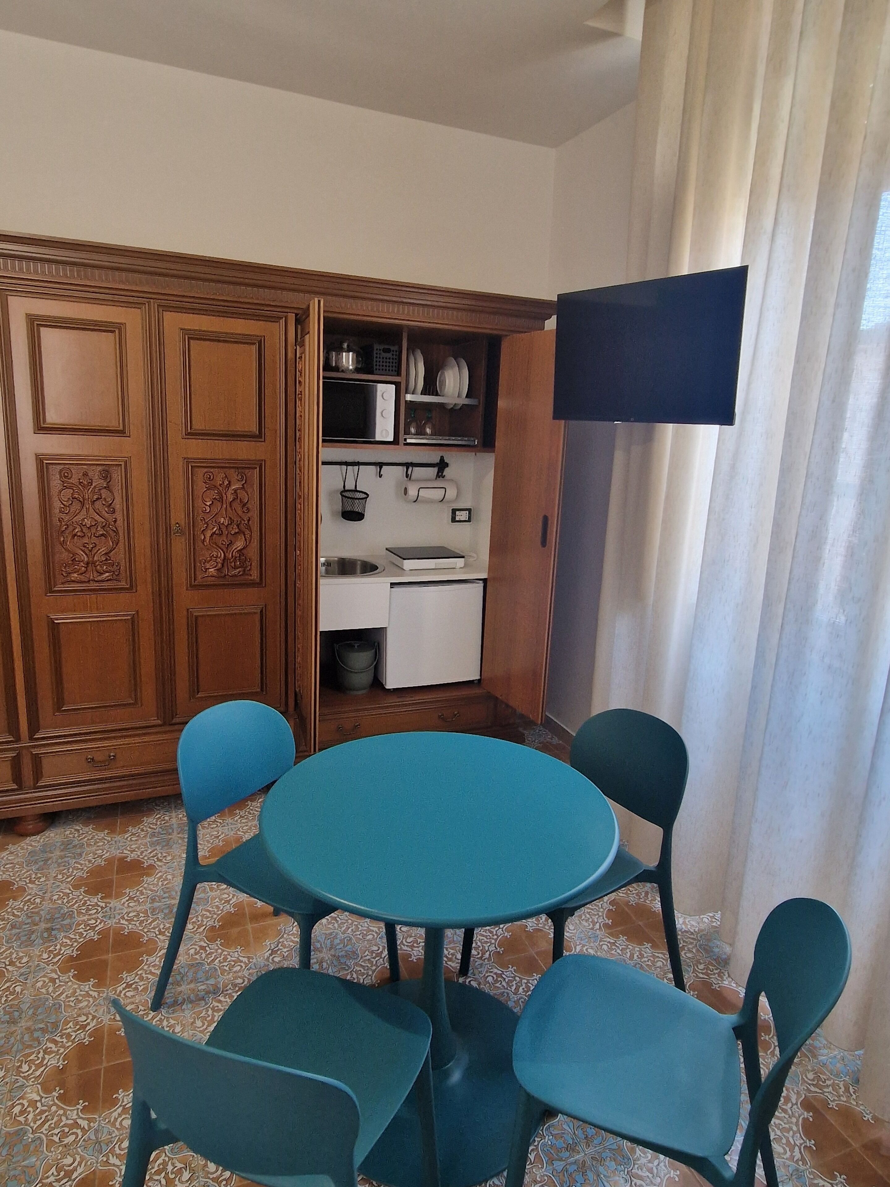Una habitación con una mesa redonda y cuatro sillas, un armario de madera con paneles decorativos, un microondas y un lavamanos pequeño.