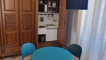 Una habitación con una mesa redonda y cuatro sillas, un armario de madera con paneles decorativos, un microondas y un lavamanos pequeño.