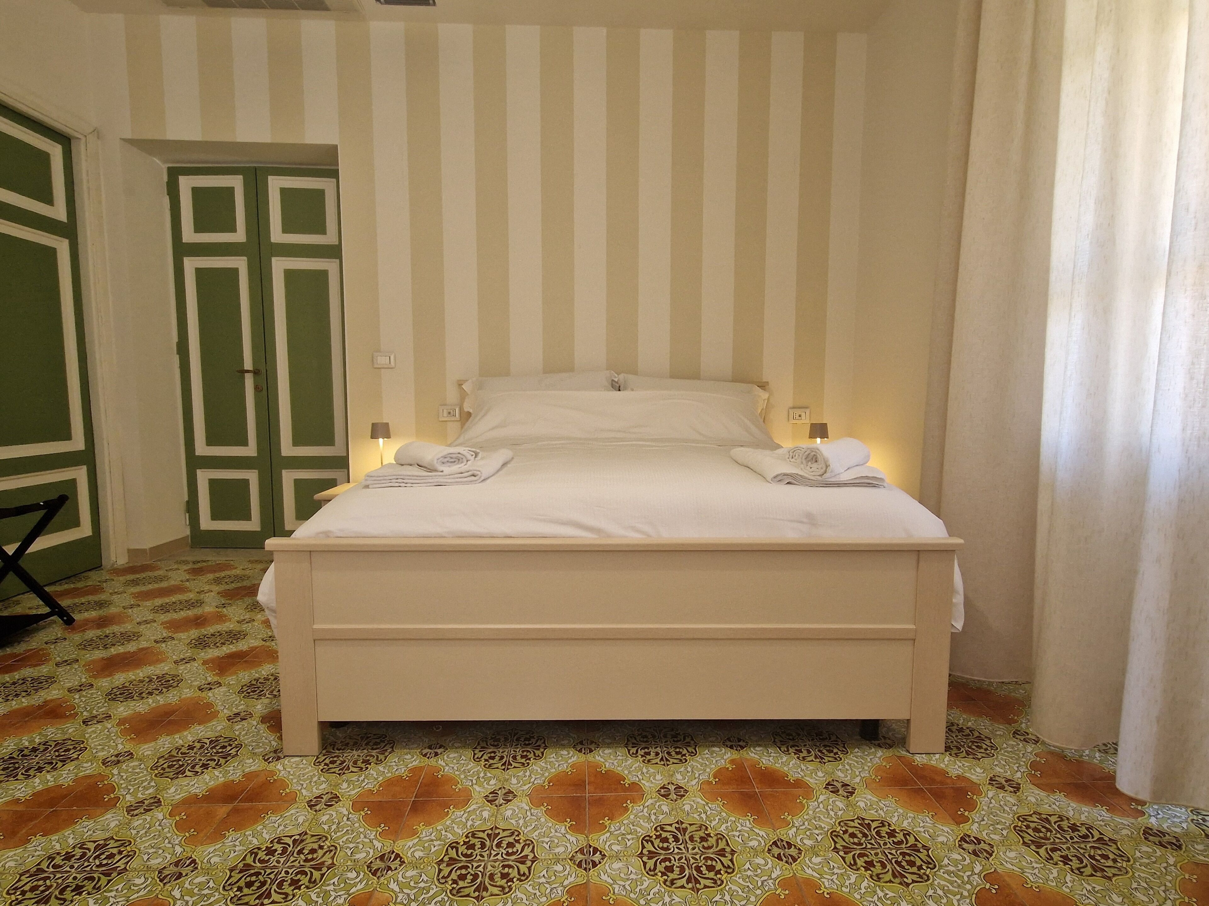 Habitación de hotel con cama, dos lámparas de noche, una puerta y baldosas de suelo con diseño.