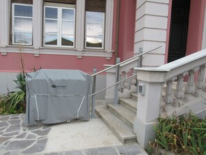 Una parrilla cubierta con el nombre de una marca, una escalera con barandilla y la fachada de un edificio con ventanas y una puerta.
